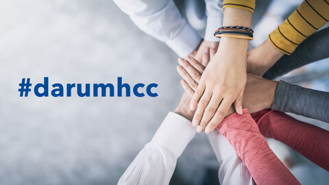 Hände berühren sich. Auf der linken Seite der Schriftzug "#darumhcc". Hände berühren sich. Auf der linken Seite der Schriftzug "#darumhcc".