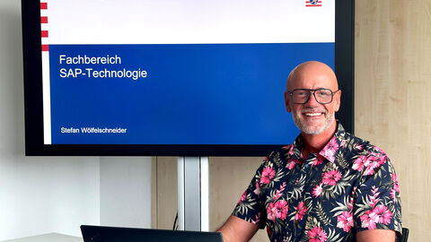 Stefan Wölfelschneider Foto von Stefan Wölfelschneider mit einem Großbildschirm im Hintergrund. Dort ist das HCC Logo und sein Name zu erkennen.